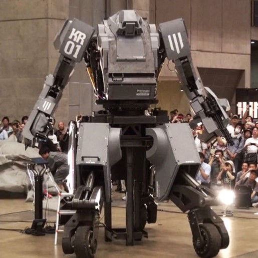 A giant grey armoured robot with KR 01 painted on one shoulder. It is much taller than the people surrounding it at the unveiling.