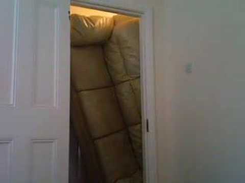 A person trying to fit a large sofa through a narrow doorway