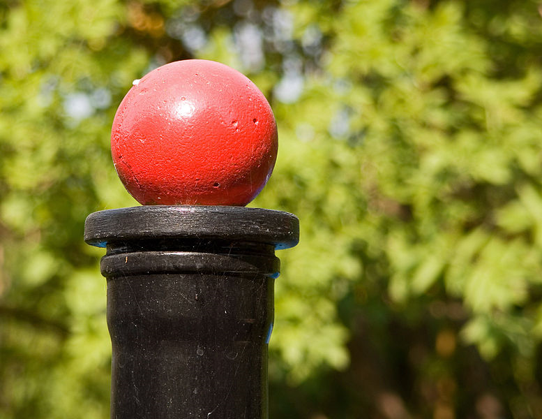 A red ball on a black post outside, with trees in the background