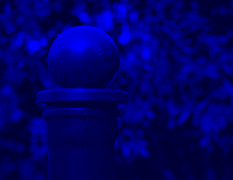 A red ball on a black post outside, with trees in the background through a blue filter
