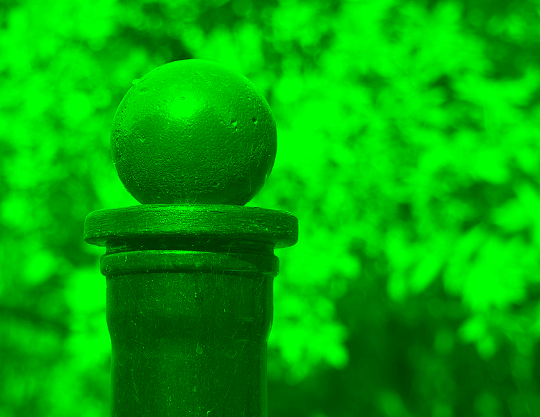 A red ball on a black post outside, with trees in the background through a green filter