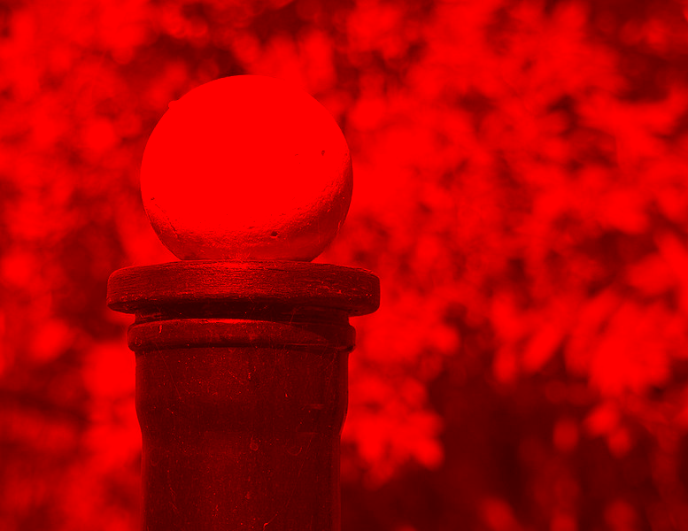 A red ball on a black post outside, with trees in the background through a red filter