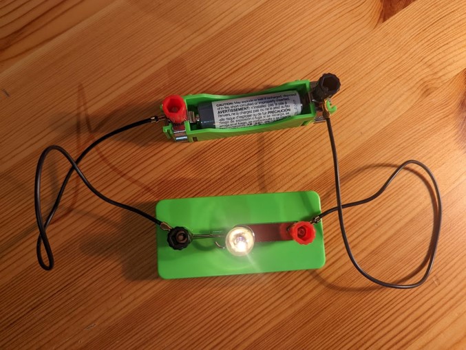 A battery connected to a lightbulb with wires.