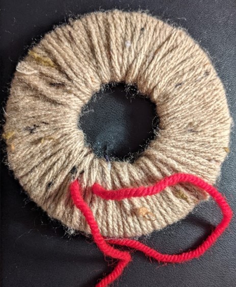 An image of the cardboard completely covered with brown wool. The only bits of the tie thread visible are the ends hanging out.